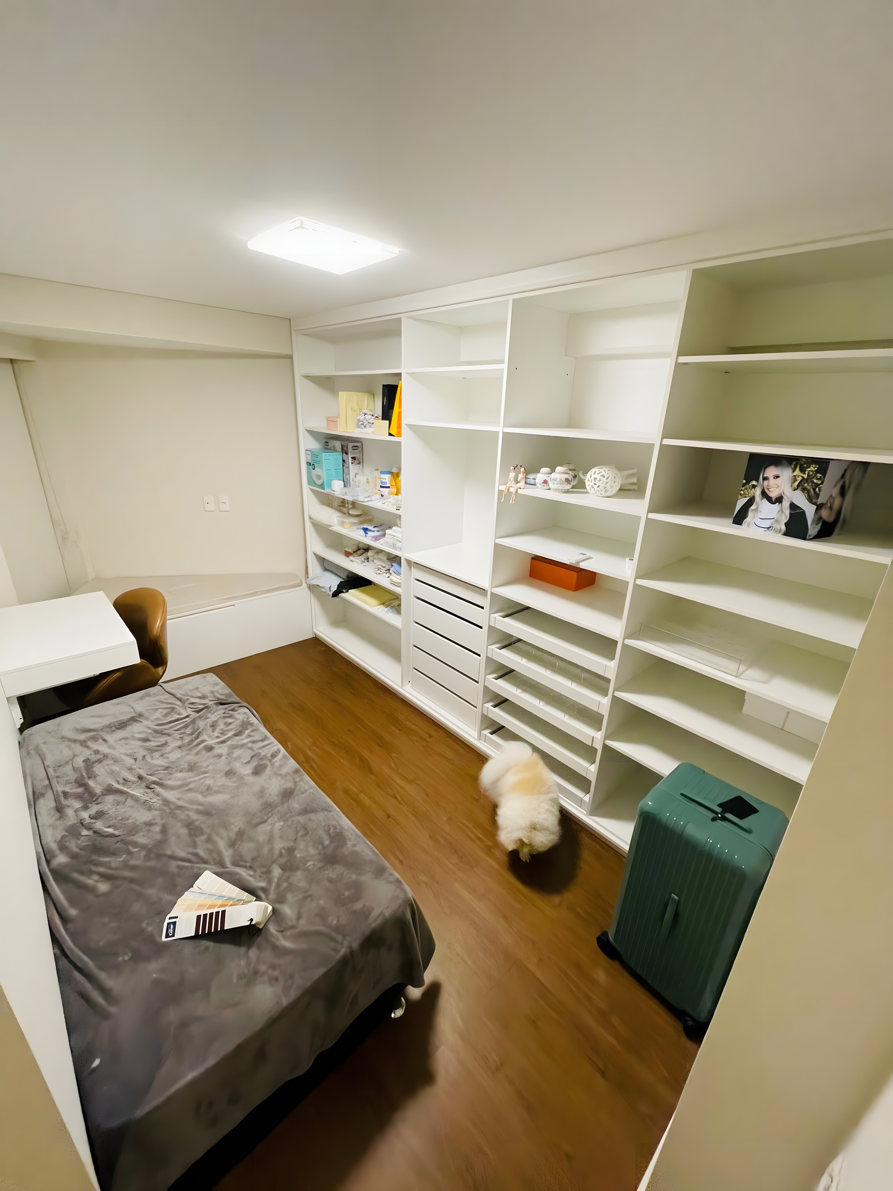 Quarto existente com estante e mala no piso
